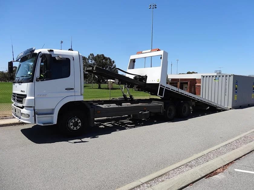 Southern Towing flatbed truck with tilt-bed ramp positioned beside a shipping container, ready for 24/7 container transport